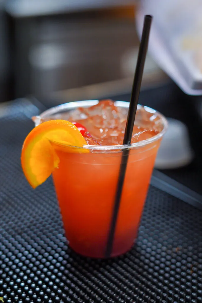 a drink with an orange garnish and two black straws